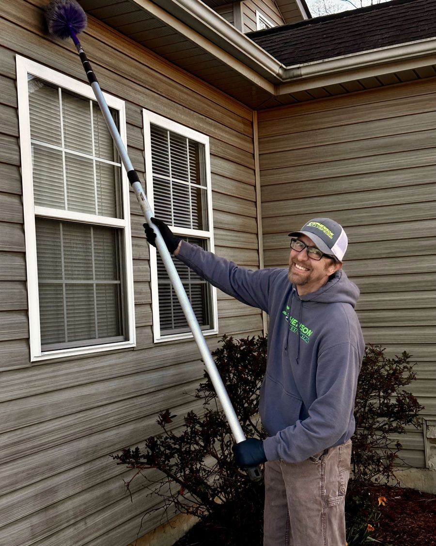 Stephenson Pest Control technician sweeping cobwebs from the eaves of a home